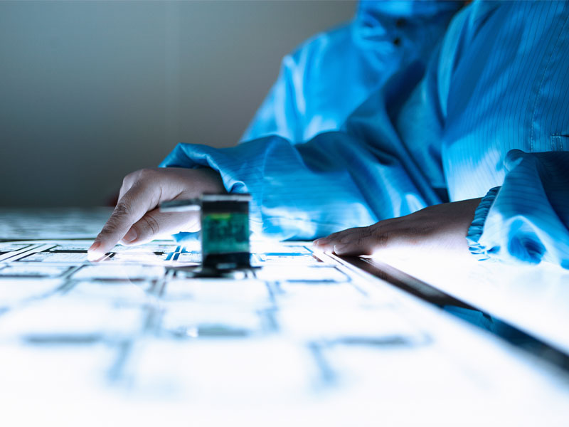 A close-up shot showing hands examining something that is on a luminous table, there is a magnifying glass next to them.